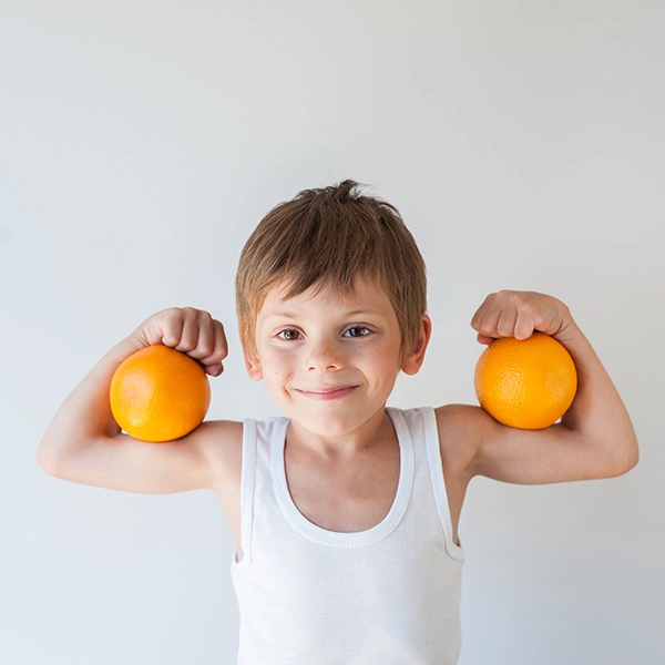 bambino che mostra i muscoli con arance in mano